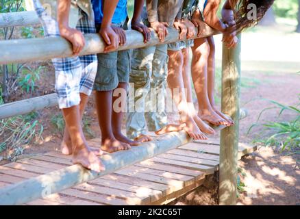 Avoir un regard curieux Vue rognée d'un groupe d'enfants en équilibre sur une clôture à l'extérieur. Banque D'Images