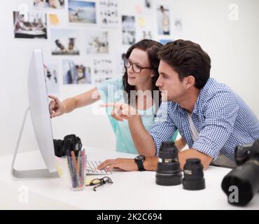 Décider de l'image parfaite Deux jeunes photographes regardent des photos sur un appareil photo numérique dans leur studio. Banque D'Images