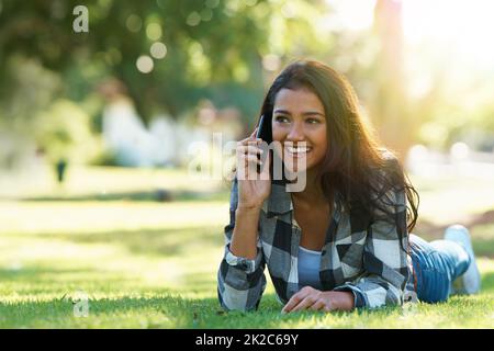 Je suis en attente dans le parc. Photo d'une jeune femme attirante parlant au téléphone dans un parc. Banque D'Images