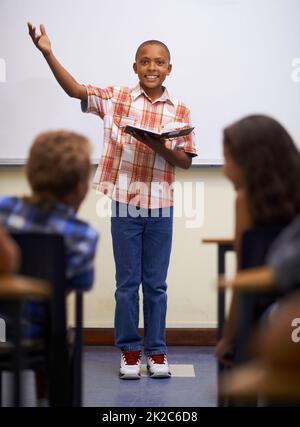 Faire sa lecture préparée. Un jeune garçon qui fait la lecture préparée à l'avant de la classe. Banque D'Images