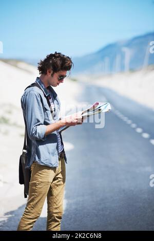 Essayer de planifier mon voyage. Jeune homme debout sur le côté de la route lisant une carte. Banque D'Images