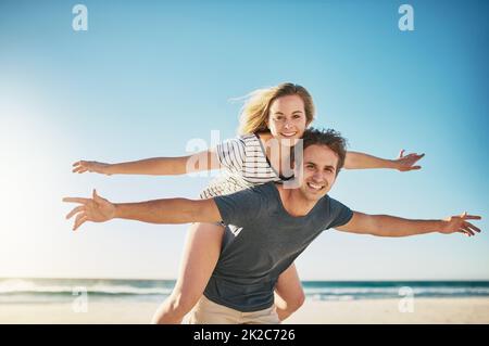 L'amour nous fait nous sentir vivants. Photo d'un jeune couple heureux en train de profiter d'une promenade en pigeyback à la plage. Banque D'Images