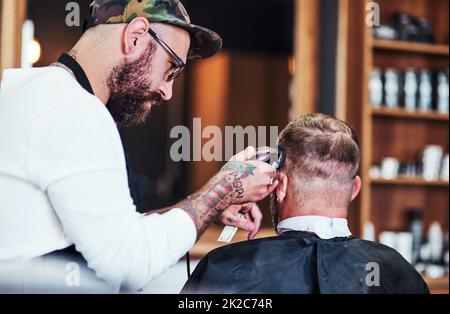 Chaque coiffure raconte une histoire. Plan court d'un beau jeune barber donnant à un client une coupe de cheveux à l'intérieur de son barbershop. Banque D'Images