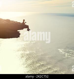 L'ascension est difficile mais la vue en vaut la peine. Photo d'un jeune homme inidentifiable admirant une vue sur l'océan depuis un surplomb de montagne. Banque D'Images