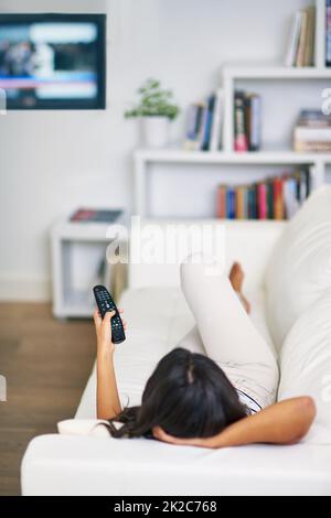 Shes mis au point. Photo d'une jeune femme regardant la télévision tout en se relaxant sur son canapé à la maison. Banque D'Images