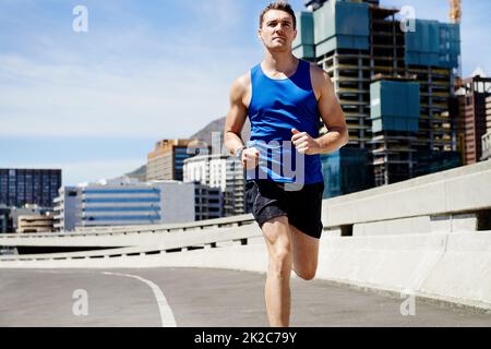 Il fixe le rythme. Un jeune homme qui garde la forme en allant courir dans la ville. Banque D'Images