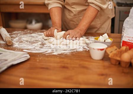 Fait avec amour Une vue rognée des mains qui travaillent la pâte tout en cuisant dans une cuisine. Banque D'Images