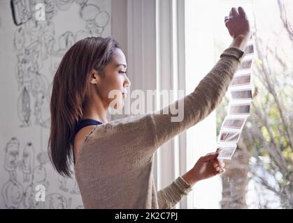 Revoir ses négatifs. Une jeune femme regardant des négatifs photographiques près d'une fenêtre. Banque D'Images