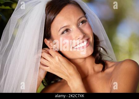 Correction des détails minuscules. Belle mariée ajustant ses boucles d'oreilles le jour de son mariage. Banque D'Images