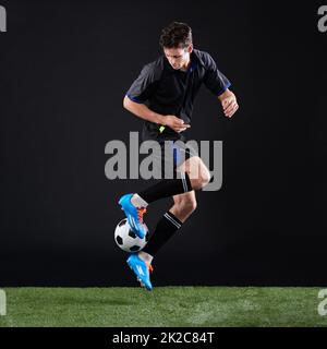 Le travail acharné bat le talent quand le talent ne travaille pas dur. Plein studio tourné d'un jeune joueur de football beau isolé sur noir. Banque D'Images