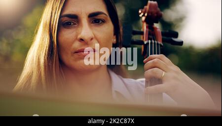 À chaque coup, elle ressent de plus en plus les notes. Photo rognée d'une belle femme jouant un violoncelle dans l'arrière-cour. Banque D'Images