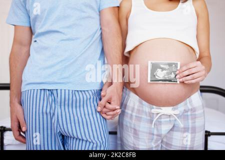 Leur premier portrait de famille. Un couple expectant tenant les mains pendant qu'elle place une photo d'échographie sur son ventre. Banque D'Images