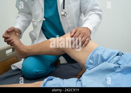Médecin asiatique physiothérapeute examinant, massant et traitement genou et jambe d'un patient senior dans la clinique orthopédique infirmière hôpital. Banque D'Images