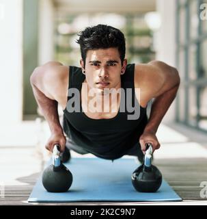 L'endurance et la discipline sont ses éléments de base. Portrait d'un jeune homme faisant des poussettes avec des haltères à la maison. Banque D'Images