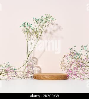 scène pour présenter des produits, des cosmétiques avec un podium rond en bois et un vase en verre avec un bouquet de fleurs Banque D'Images