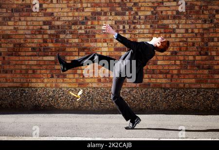 Theres une peau de banane potentielle dans chaque entreprise d'affaires. Un jeune homme glissant sur une peau de banane. Banque D'Images