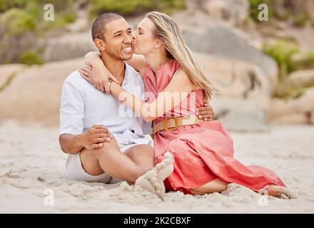 Baiser, l'amour et le couple sur le sable de plage avec le sourire heureux pour les vacances ou les vacances ensemble. Le bonheur sain et l'homme et la femme interraciales ou les gens se détendent Banque D'Images