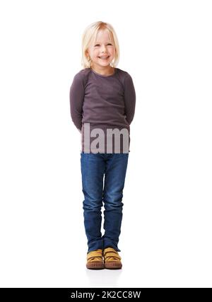 C'est un enfant charmant. Portrait complet d'une petite fille souriant et debout sur un fond blanc avec les mains derrière son dos. Banque D'Images