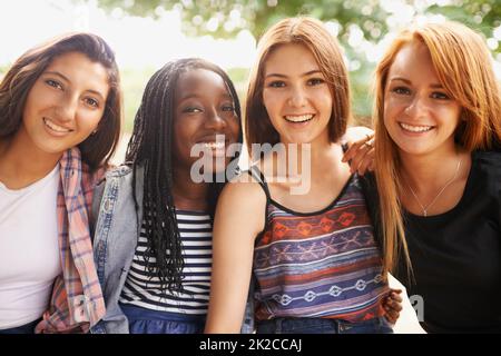 L'arc-en-ciel de cette nation. Quatre belles jeunes filles souriant se sont heureuses pendant qu'elles s'assoient à l'extérieur. Banque D'Images
