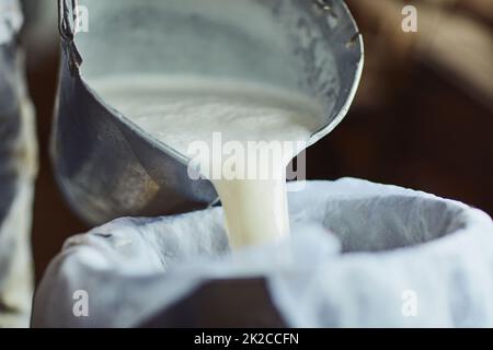 Les étapes pour faire du fromage. Prise de vue d'un fermier mâle méconnaissable versant du lait non transformé dans un récipient à l'intérieur d'une grange. Banque D'Images