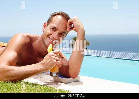 Détente au bord de la piscine. Portrait d'un homme souriant qui profite du soleil près de la piscine tout en tenant un verre. Banque D'Images