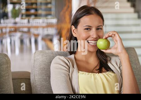 En forme et en sensation. Portrait d'une jeune femme attrayante mangeant une pomme tout en se relaxant sur un canapé. Banque D'Images