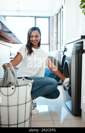 Faire le linge avant qu'il ne s'accumule. Prise de vue d'une jeune femme utilisant un lave-linge à la maison. Banque D'Images