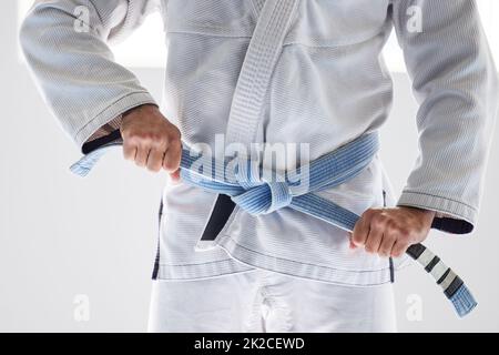 HES n'est plus un amateur. Coupe courte d'un artiste martial masculin méconnu qui attache sa ceinture à la salle de sport. Banque D'Images