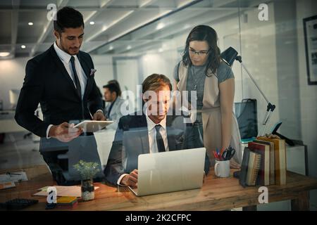 Augmentation de la productivité grâce au travail d'équipe et aux heures supplémentaires. Prise de vue d'une équipe de collègues utilisant un ordinateur portable lors d'un quart de nuit au travail. Banque D'Images