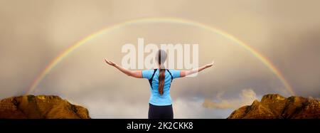 À un à l'intérieur et avec la nature. Une femme debout avec ses bras tendus devant un arc-en-ciel. Banque D'Images