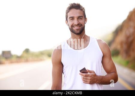 Sélection d'un album pour l'accompagner lors de sa course. Portrait d'un beau jeune homme debout à l'extérieur avec un joueur de MP3. Banque D'Images