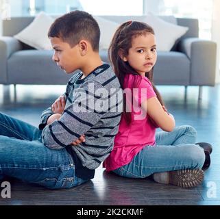 Ils ont tous les deux été envoyés au coin méchant. Photo de deux jeunes enfants méchants assis sur le sol avec leurs dos tournés l'un vers l'autre à la maison. Banque D'Images