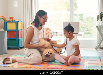 Kindergarten, education and stethoscope with teacher and girl playing doctor game with teddy bear for development, learning and care. Classroom Stock Photo