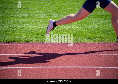 Jambe et ombre de la course de coureur sur terrain de sport avec fond d'herbe Banque D'Images