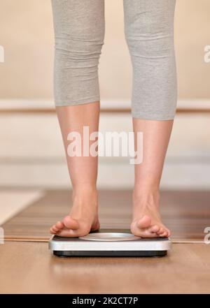 Ces chiffres sont enfin en baisse. Gros plan d'une jeune femme qui se pèse sur une balance à la maison. Banque D'Images