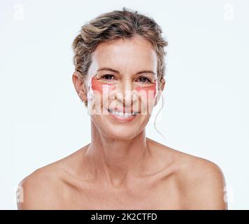 Il garde mes yeux à l'air jeune, ferme et en bonne santé. Photo d'une femme mûre portant des plaques de gel sous les yeux tout en posant sur un fond blanc. Banque D'Images