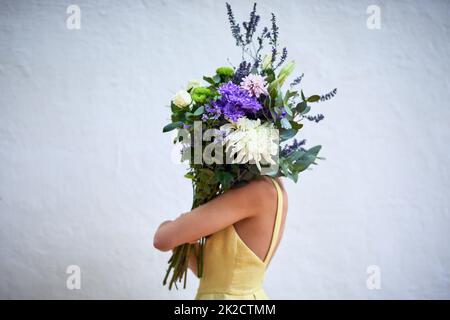 Faire partie de la nature. Photo en studio d'une femme méconnaissable portant un bouquet de fleurs sur fond gris. Banque D'Images