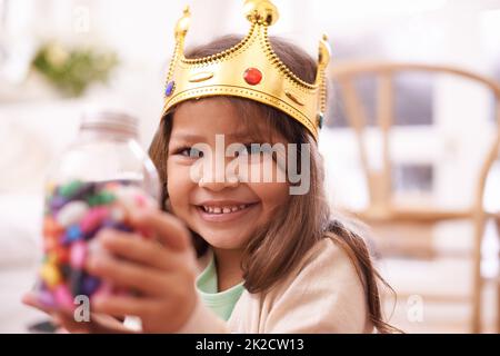 Reine de son imagination. Une petite fille mignonne habillée comme une princesse tout en mangeant des bonbons à la maison. Banque D'Images