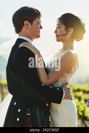 Maintenant et pour toujours mon cher. Photo d'une jeune mariée et d'un marié joyeux se tenant les uns les autres tout en regardant l'extérieur de l'œil à l'œil pendant la journée. Banque D'Images