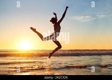 Vous êtes libre d'être qui que ce soit. Photo d'une jeune femme qui saute en plein air contre un beau coucher de soleil sur la plage. Banque D'Images