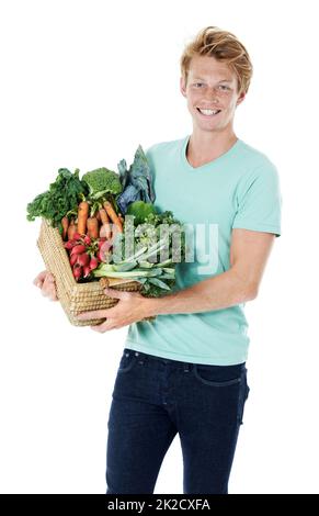 Frais de la ferme. Un jeune homme souriant à tête rouge tenant un panier rempli de légumes frais biologiques. Banque D'Images