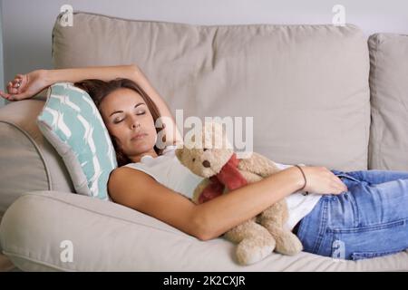 Même la maman a parfois besoin d'une sieste. Une jeune mère épuisée s'endormit rapidement sur le canapé avec son ours en peluche dans la main. Banque D'Images