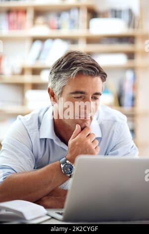 Let me think about this. a handsome mature man lying on his living room floor using a laptop. Stock Photo