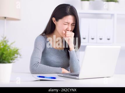 Une jeune femme malade qui s'occupe d'un ordinateur portable tousse lutte contre le coronavirus ou la grippe sur le lieu de travail Banque D'Images