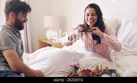 C'est pourquoi je l'ai marié. Photo d'une jeune femme prenant une photo du petit déjeuner que son mari lui a servi au lit. Banque D'Images