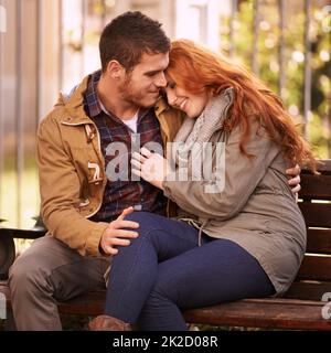 Le cœur qui aime est toujours jeune. Photo d'un jeune couple heureux partageant un moment affectueux sur un banc de parc. Banque D'Images