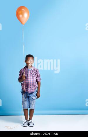 Regardez ce que j'ai obtenu. Photo d'un jeune garçon tenant un ballon sur un fond bleu. Banque D'Images