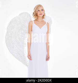 Son innocence est lumineuse. Photo studio d'une jeune femme dans des ailes d'ange isolées sur blanc. Banque D'Images