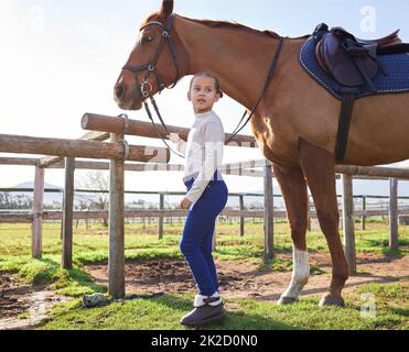 Une petite fille et son cheval. Photo pleine longueur d'une adorable jeune fille debout avec son cheval à l'extérieur sur le ranch. Banque D'Images