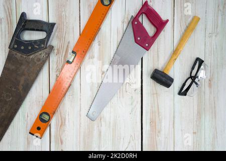 L'équipement de travail du bois est soigneusement organisé sur le plancher en bois. Commandé comme suit, ancienne scie pleine de rouille, niveau d'aluminium magnétique orange, scie à main rouge, maillet jaune, lunettes anti-poussière noires. Banque D'Images